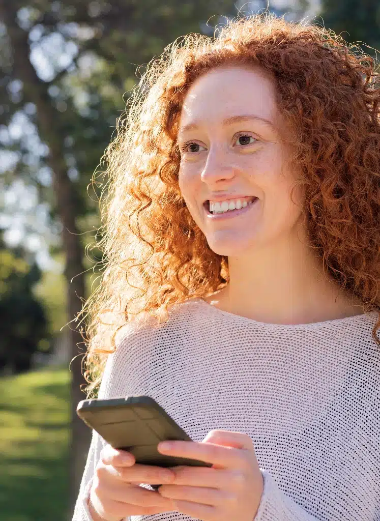 woman around trees holding a phone